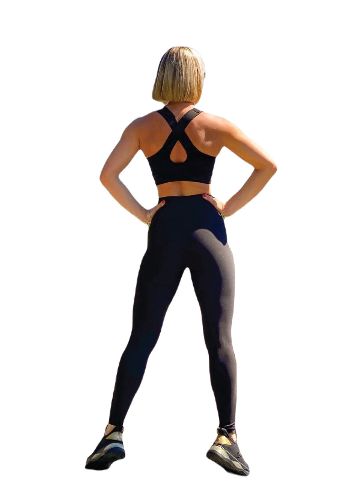 Eine Person mit Bob-Haarschnitt in einem Lismina 101 Single Crossed Sport Bra in Schwarz und Leggings, die Hände in die Hüften gestemmt und mit dem Gesicht abgewandt.
